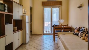 A compact room with a bed, a small table, a chair, a refrigerator, and a window with curtains. - Loving Gift - Giardini Naxos (Giardini Naxos)
