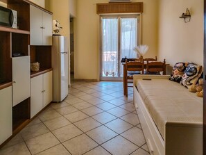 A compact room with a bed, a small table, a chair, a refrigerator, and a window with curtains. - Loving Gift - Giardini Naxos (Giardini Naxos)