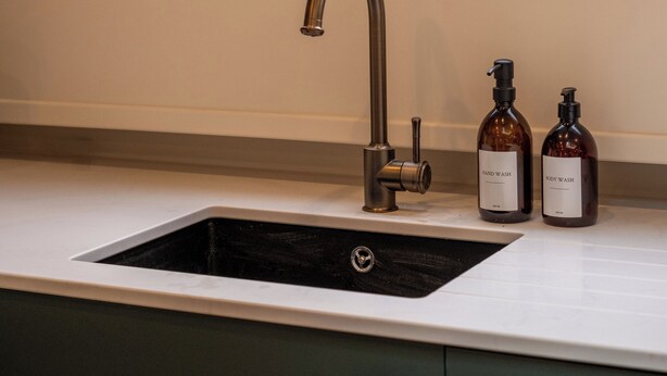 A kitchen with a window, a sink, and two hand wash bottles. - Gainsborough Boat House (London)