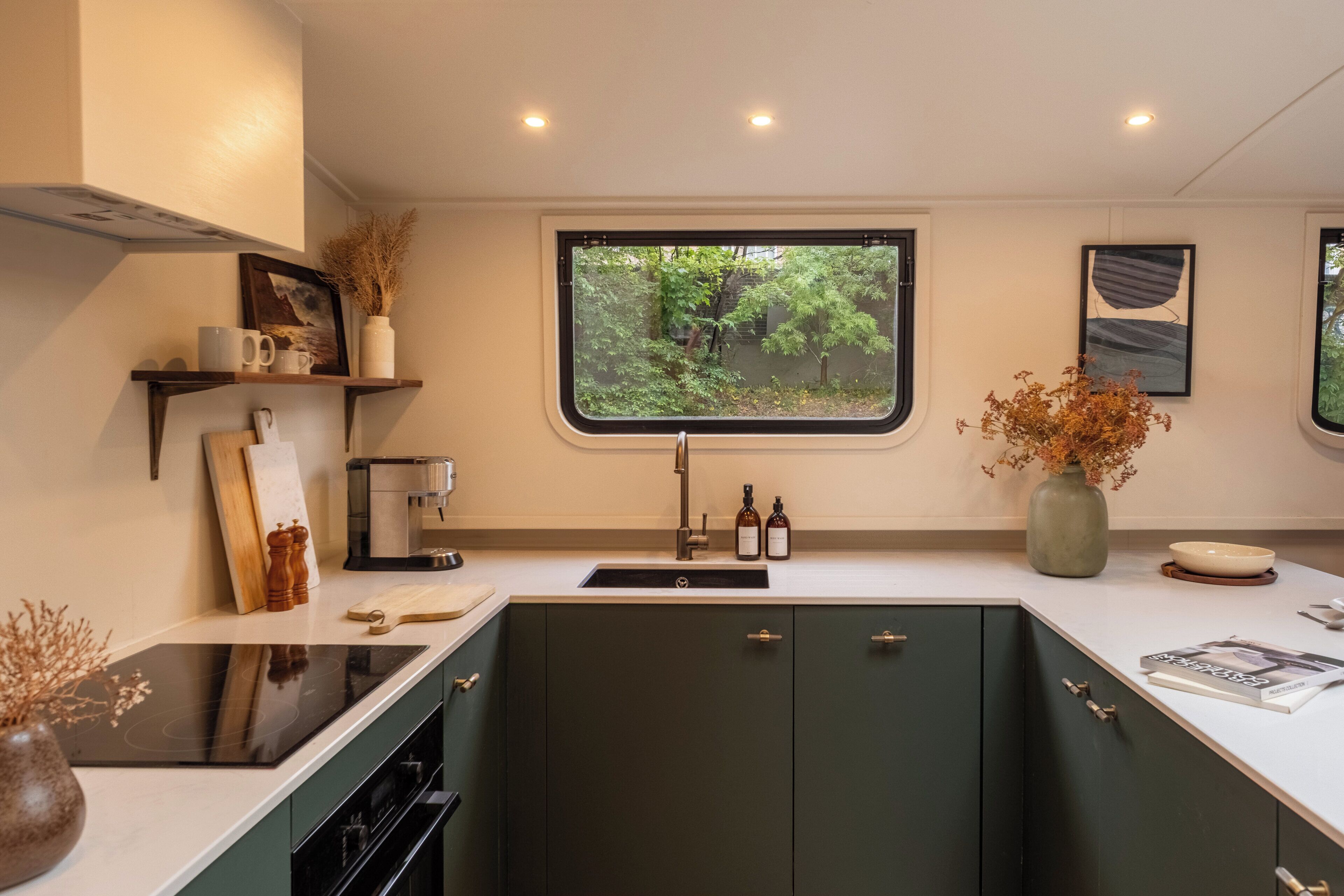 A modern kitchen with a built-in stove, a window with a view of greenery, and a coffee machine.