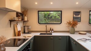 A modern kitchen with a built-in stove, a window with a view of greenery, and a coffee machine. - Gainsborough Boat House (London)