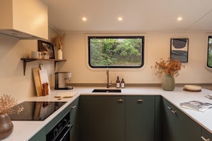 A modern kitchen with a built-in stove, a window with a view of greenery, and a coffee machine.