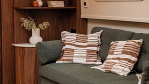 A cozy living area with a green sofa, striped pillows, a wooden bookshelf, and a window with a view. - Gainsborough Boat House (London)
