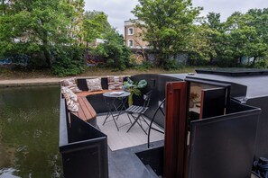 A modern outdoor seating area with a table and chairs, a small garden, and a view of the river.