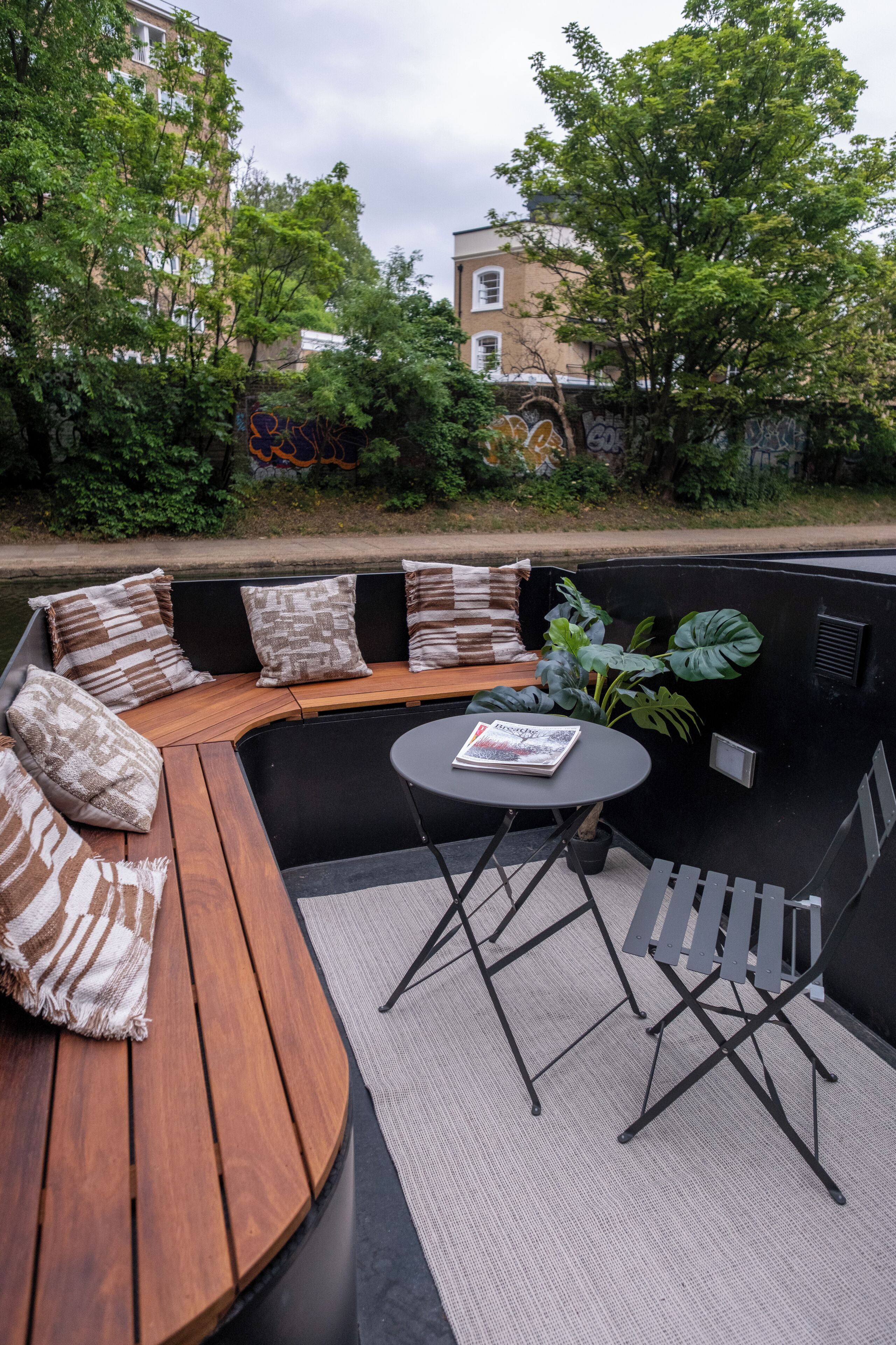 An outdoor seating area with a curved wooden bench, cushioned seating, a round table, and a magazine.