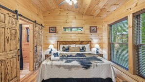 A wooden cabin bedroom with a bed, two bedside tables, a ceiling fan, and a window with blinds. - Bearly Behaving: Smoky Mountain Cabin Escape (Sevierville)
