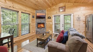 A log cabin interior with a fireplace, wooden walls, a sofa, and a dining area. - Bearly Behaving: Smoky Mountain Cabin Escape (Sevierville)