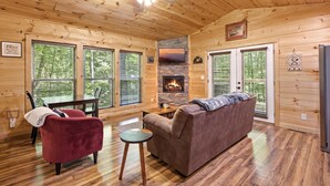 A wooden cabin interior with a fireplace, a red armchair, a brown sofa, and a dining table. - Bearly Behaving: Smoky Mountain Cabin Escape (Sevierville)