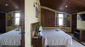 Ein Hotelzimmer mit zwei Betten, einer Ziegelwand, einem Fernseher und einem Fenster mit Vorhängen.