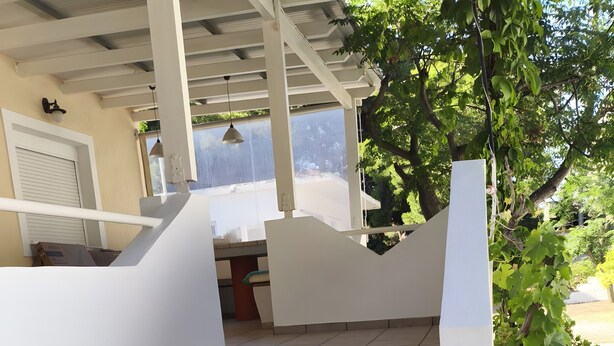 Un escalier extérieur mène à un espace abrité, avec un mur blanc et un arbre.