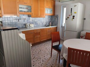 A compact kitchen with wooden cabinets, a white refrigerator, a sink, and a dining table with chairs. - Holiday Home 'Nicks House By Zarkco' with Private Terrace, Wi-Fi and Air Conditioning (Artemida)