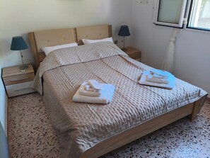 A neatly made bed with a textured blanket, two bedside lamps, and a window with a curtain. - Holiday Home 'Nicks House By Zarkco' with Private Terrace, Wi-Fi and Air Conditioning (Artemida)