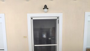 Une porte dotée d’un panneau en verre dépoli, un paillasson noir à l’entrée et un luminaire fixé au mur.