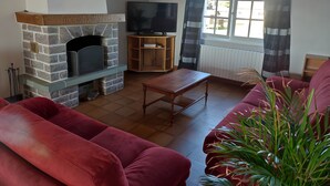 A living room with a stone fireplace, a television, a wooden coffee table, and a red sofa. - Holiday Home “Gîte for 10 in Barfleur” with Private Terrace, Garden & Wi-Fi (Barfleur)