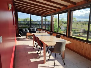 Ein moderner Essbereich mit einem Holztisch und Stühlen, einer Couch und großen Fenstern mit Blick ins Freie.
