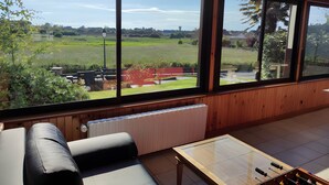 A room with a large window, a sofa, a table with a foosball table, and a radiator. - Holiday Home “Gîte for 10 in Barfleur” with Private Terrace, Garden & Wi-Fi (Barfleur)