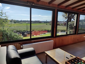 Ein Zimmer mit einem großen Fenster, einer Couch, einem Tisch mit einem Kicker und einer Heizung.