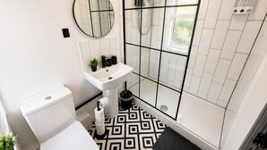 A bathroom with a toilet, sink, mirror, shower, and patterned floor. - 6-bed House - Sleeps 11 - Garden - Parking (Sheffield)