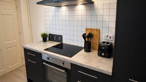 A modern kitchen with a black stove, a toaster, and a wooden cutting board. - 6-bed House - Sleeps 11 - Garden - Parking (Sheffield)