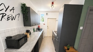 A modern kitchen with a microwave, sink, and cabinets. - 6-bed House - Sleeps 11 - Garden - Parking (Sheffield)