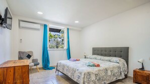 Ein Schlafzimmer mit einem Bett, einem Schreibtisch, einem Stuhl, einem Fenster mit Vorhängen und einer Klimaanlage.
