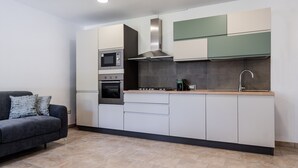 Eine moderne Küche mit integriertem Backofen, Mikrowelle und Herd, ein graues Sofa mit gemusterten Kissen und ein Fliesenboden.