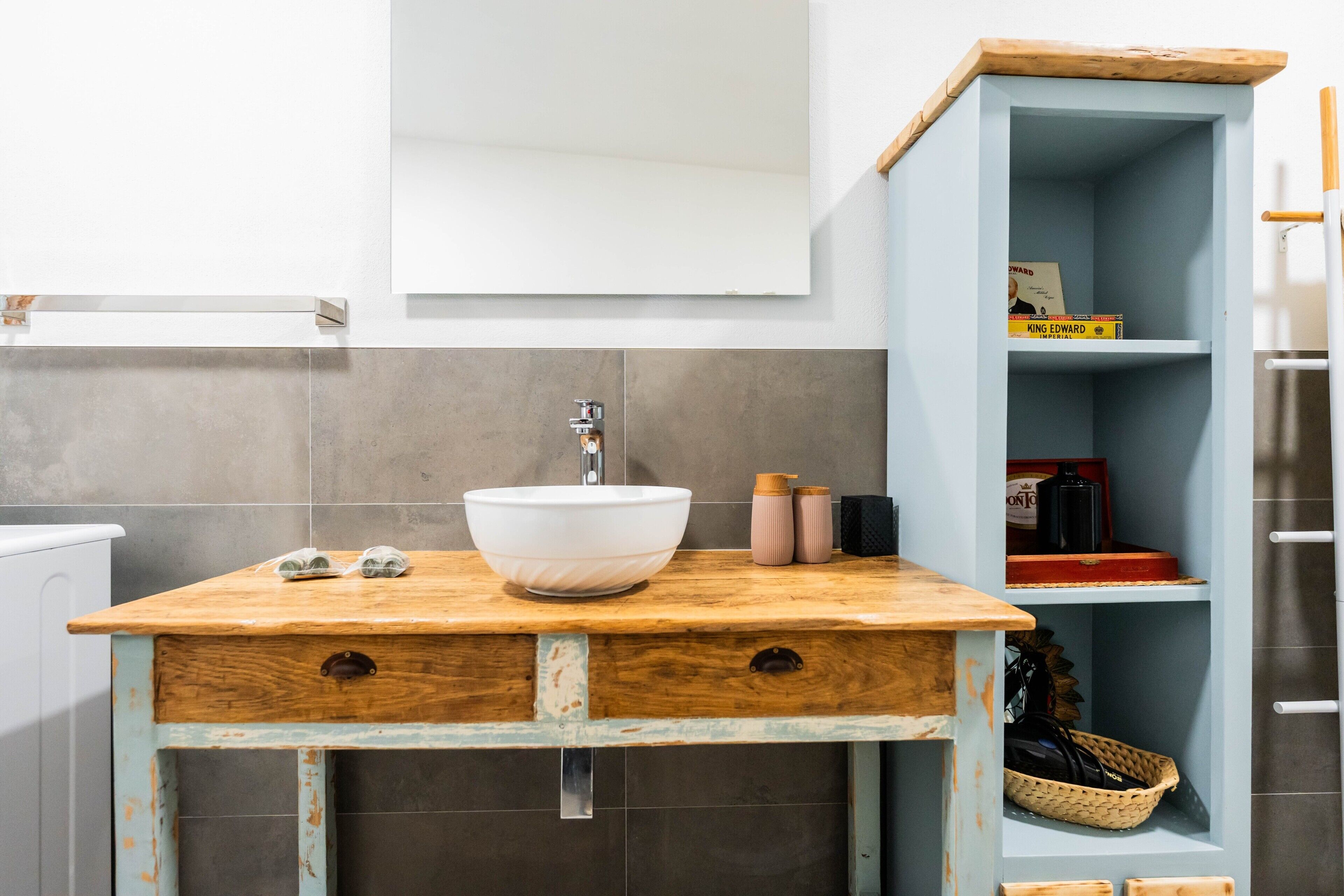 A bathroom with a white sink, wooden vanity, and a blue shelving unit with books and toiletries.