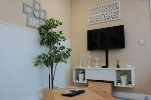 Una sala de estar con televisor, una planta, chimenea y decoración en las paredes.