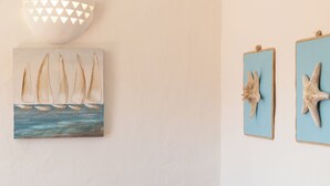 Una habitación con un sofá azul, una lámpara de pared y dos cuadros con barcos a vela y estrellas de mar.