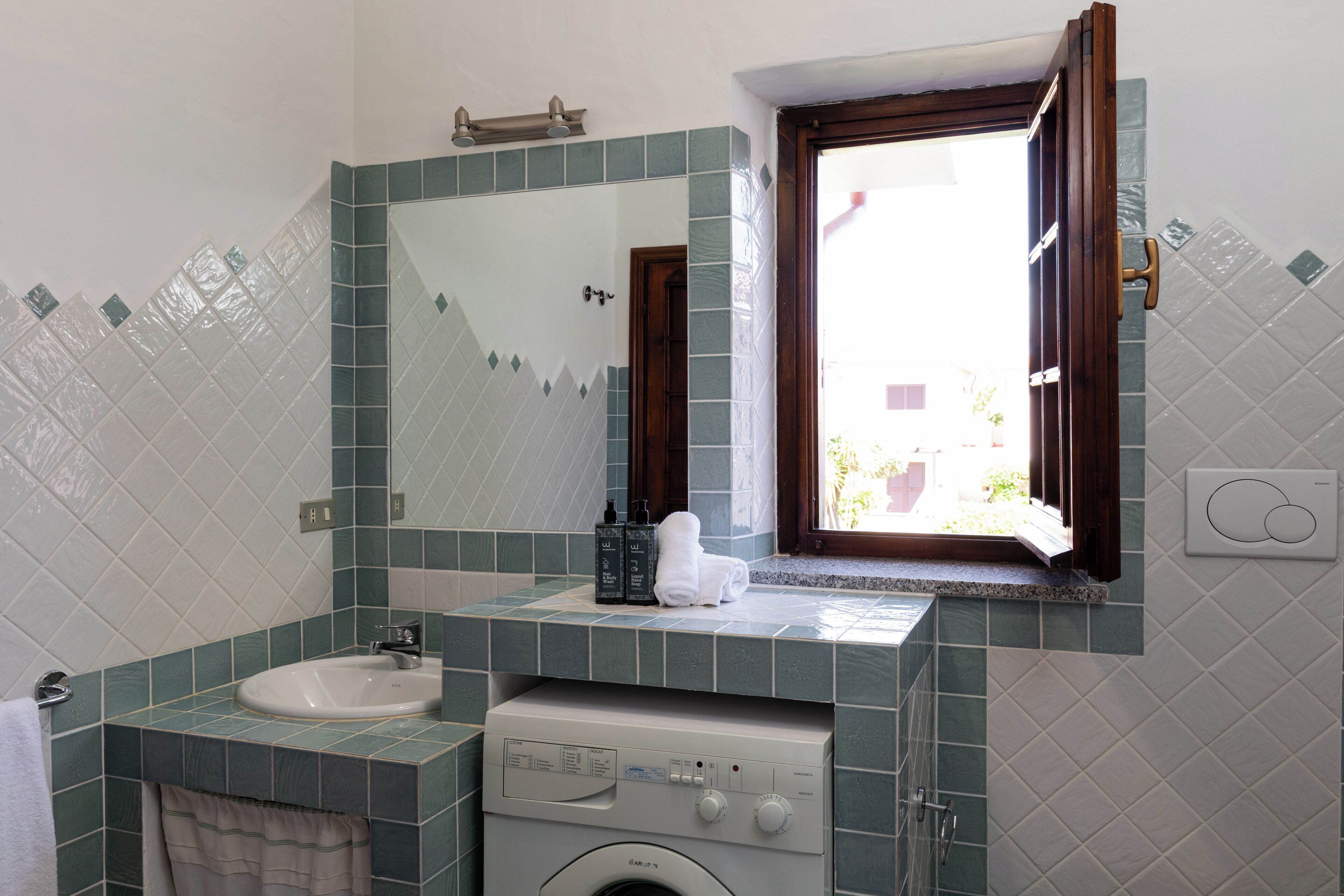 A bathroom with a sink, mirror, window, and washing machine.