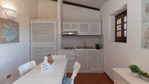 Una cocina compacta con armarios blancos, una mesa de comedor con sillas y un ventanal pequeño.