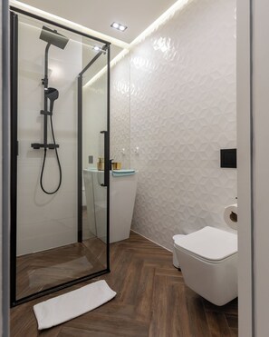 Et moderne badeværelse med en glasafskærmet bruseniche, et hvidt toilet og trægulv.