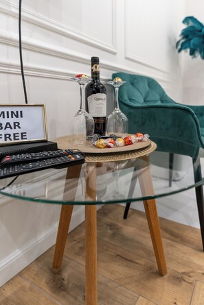 Une table avec un plateau en verre, une bouteille de vin, un verre et une assiette de collations. Une pancarte indique : « MINI-BAR – À DISPOSITION GRATUITEMENT ».