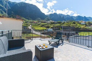 Eine Terrasse mit Gartenmöbeln, einem Tisch mit Tellern und Gläsern und Blick auf eine gebirgige Landschaft.