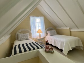 A bedroom with two beds, a window with curtains, a nightstand with a lamp, and a decorative lighthouse. - DRIFT INN COTTAGE-1 mile from Port Clyde & Walk to Drift Inn Beach, Dog-Friendly (St. George)