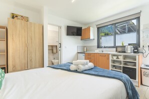 Quarto de hotel compacto com cama, pequeno espaço de cozinha, banheiro e guarda-roupa.