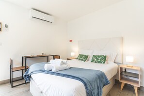 Ein Hotelzimmer mit einem Bett, Nachttischen, einem Schreibtisch, einer Klimaanlage und einem wandmontierten Thermostat.
