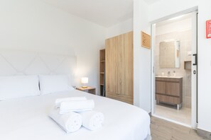 Ein Hotelzimmer mit einem Bett, einem Nachttisch, einem Holzschrank und einem durch eine geöffnete Tür einsehbaren Badezimmer.