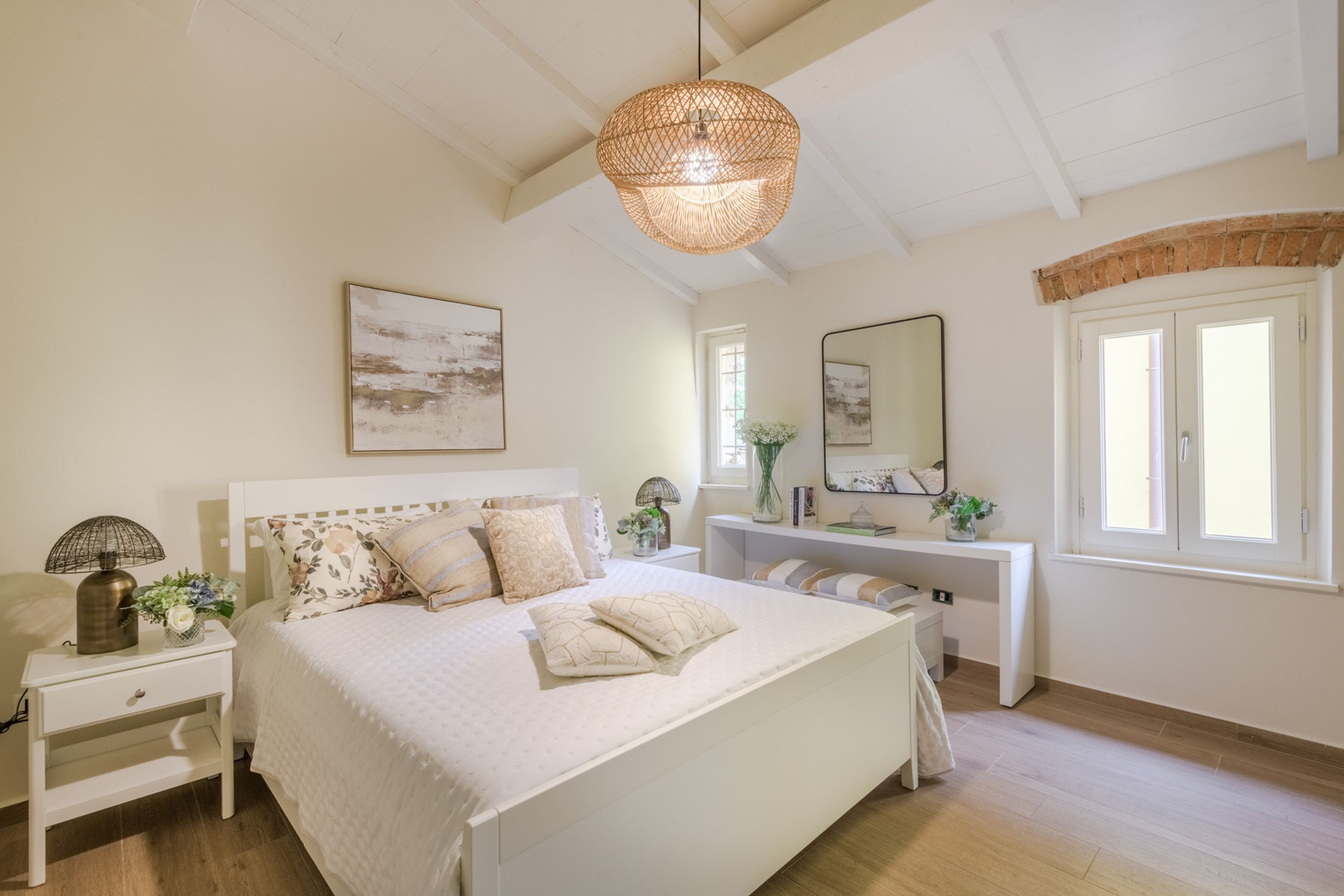 Ein Schlafzimmer mit einem großen Bett, Nachttischen, einem Schreibtisch, einem Spiegel und einer Pendelleuchte.