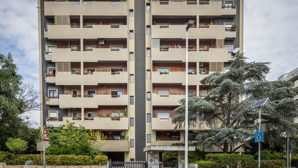A multi-story residential building with balconies, a gated entrance, and a pedestrian crossing sign. - GuestHost - La Pavoncella Terrace Apartment (Cagliari)
