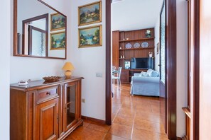 A hallway with a wooden cabinet, a mirror, and two framed paintings. - GuestHost - La Pavoncella Terrace Apartment (Cagliari)