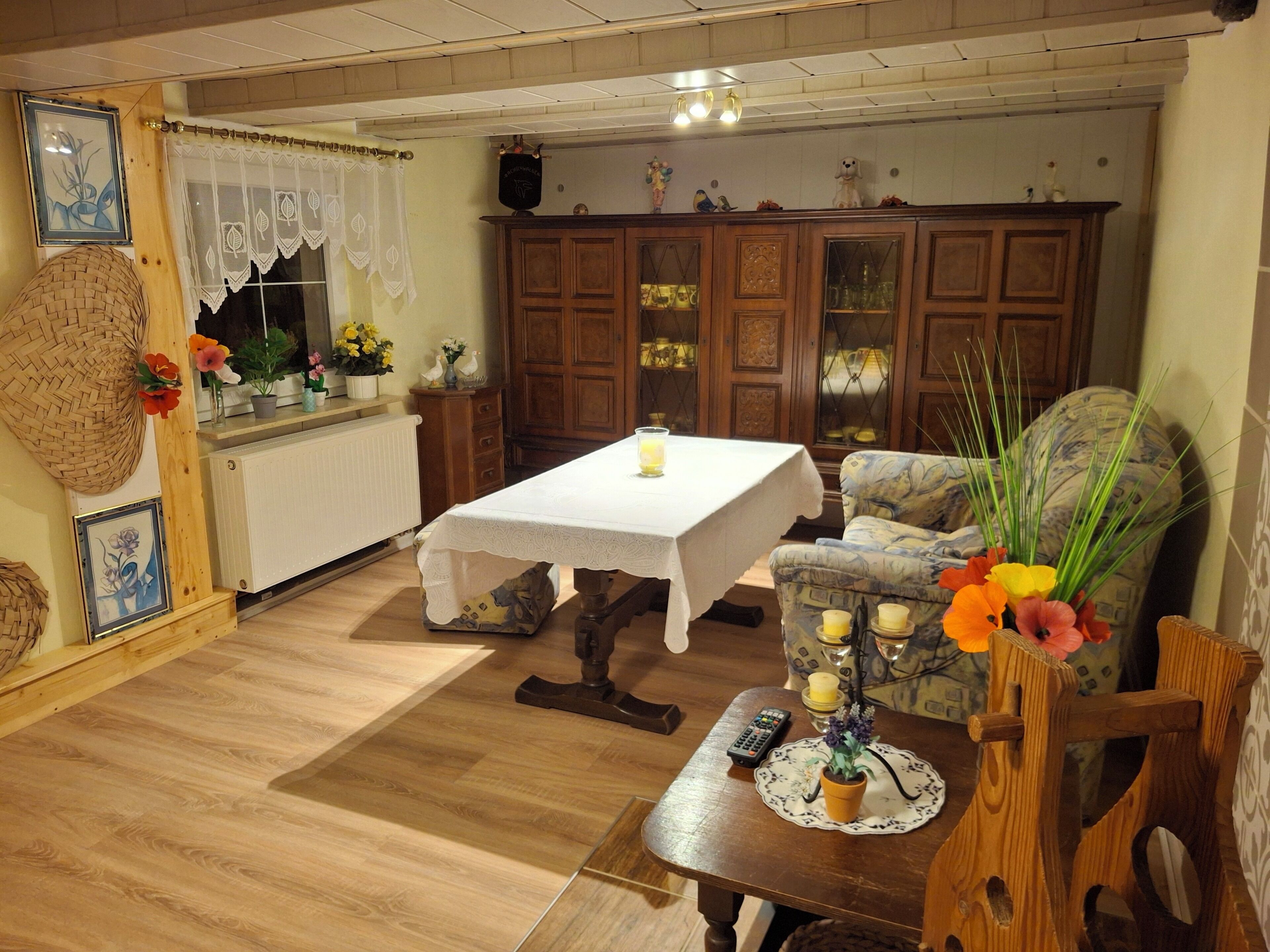 A cozy room with a wooden table, a cushioned chair, a radiator, and a cabinet with glass doors.. Haus Semmelrodt small vacation home between the castles Ludwigstein and Hanstein