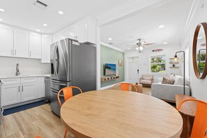Eine moderne Küche mit weißen Schränken, einem Edelstahl-Kühlschrank und einem Essbereich mit einem runden Holztisch und orangefarbenen Stühlen.