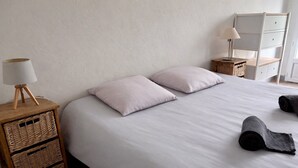 Une chambre à coucher comprenant un lit, deux oreillers, une lampe de chevet, une table de chevet avec des paniers et une commode avec un miroir.