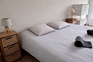 Ein Schlafzimmer mit einem Bett, zwei Kissen, einer Nachttischlampe, einem Nachttisch mit Körben und einer Kommode mit Spiegel.
