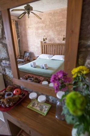 A room with a wooden bed, a ceiling fan, a mirror, and a small table with a vase of flowers.