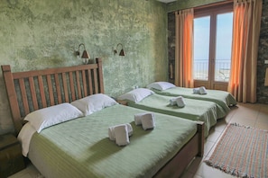 A room with two beds, a wooden headboard, a green wall, a window with curtains, and a woven rug.