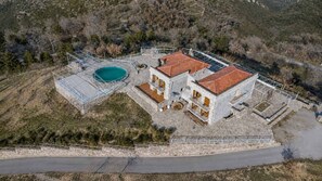 Un bĂątiment Ă deux Ă©tages dotĂ© dâune piscine, entourĂ© dâun mur en pierre et dâune zone dallĂ©e.