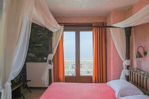 Une chambre Ă coucher avec un lit, une fenĂȘtre avec des rideaux, un radiateur et une vue sur la mer.