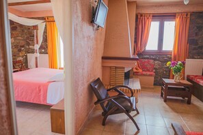 Una habitación con cama, televisión, chimenea y una zona de estar con mesa y sillas.